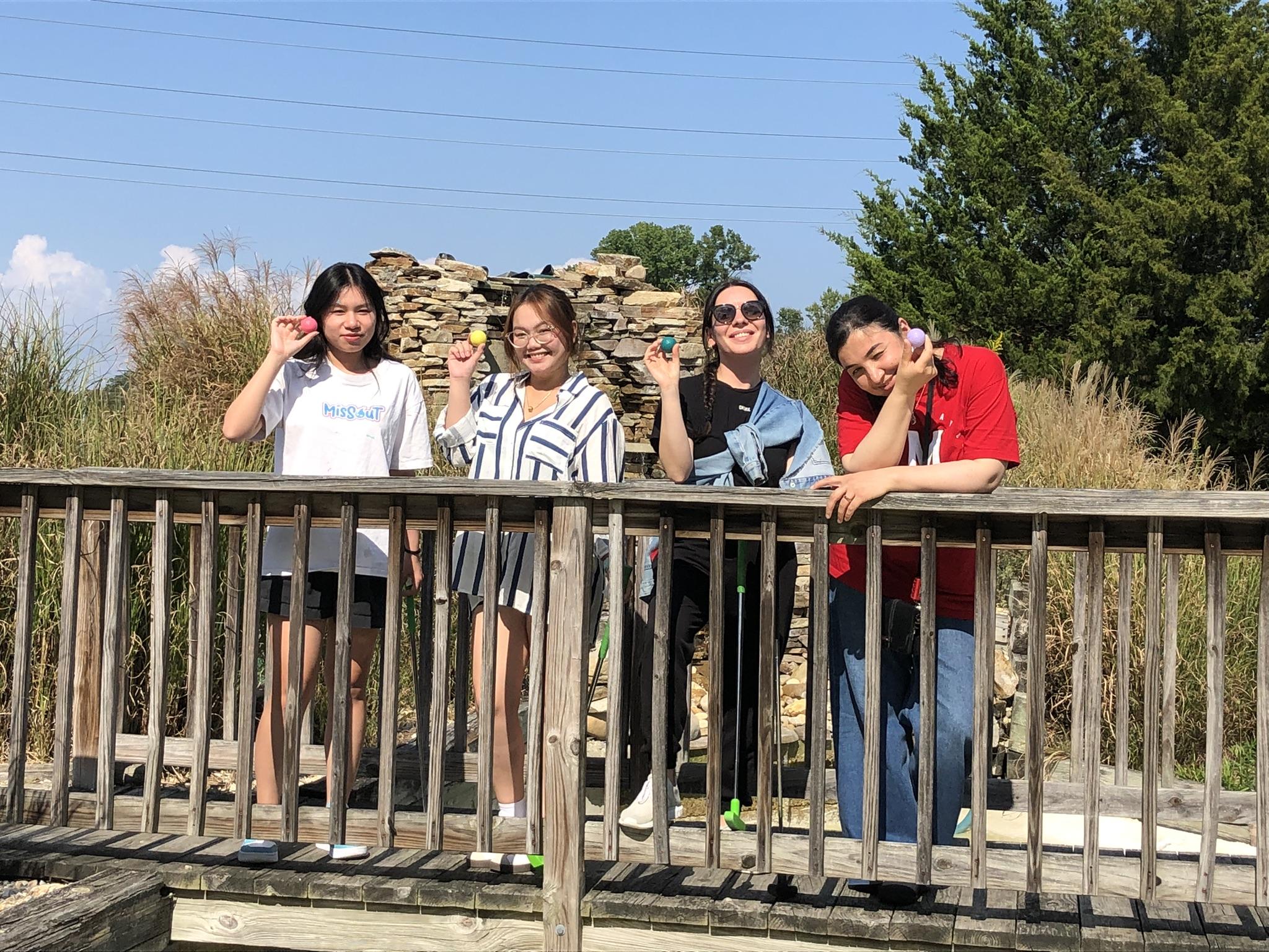 Four students smiling, leaning over an outdoor railing