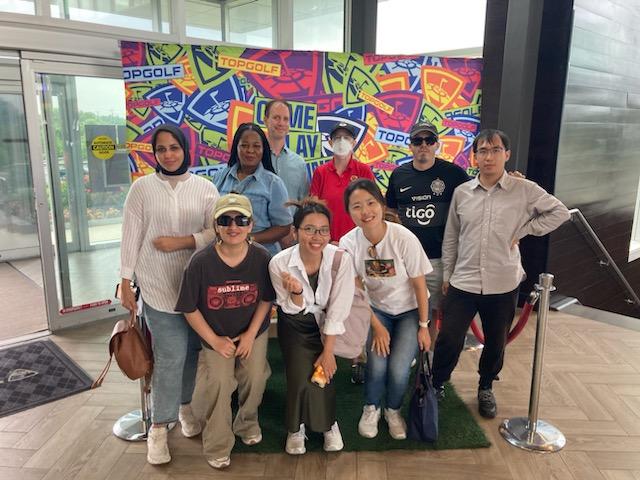Students and professors posing in front of an entrance with a colorful backdrop